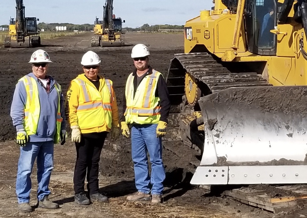 Three construction workers beside a backhoe